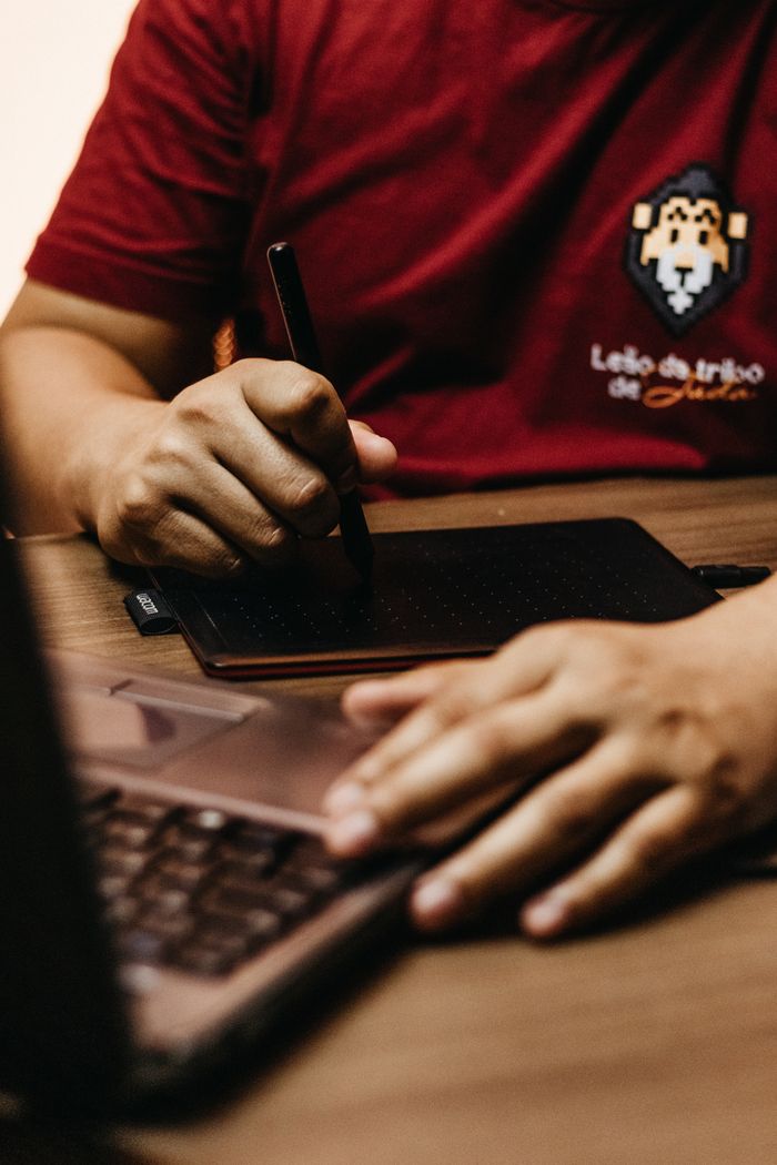 Close-up of a designer using a graphic tablet and laptop at a desk in an office.
