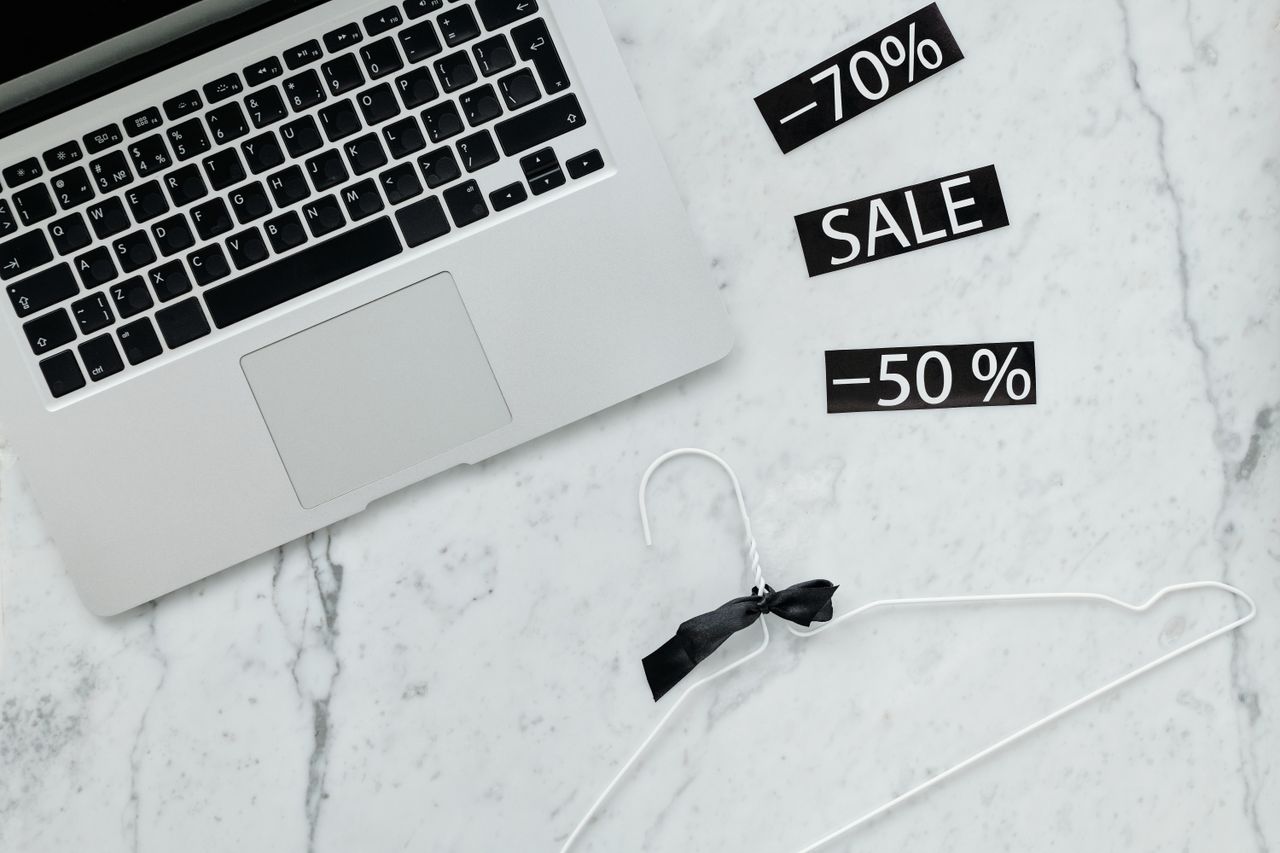 Flat lay of a laptop, hanger, and sale stickers on a marble desk, ideal for Black Friday themes.