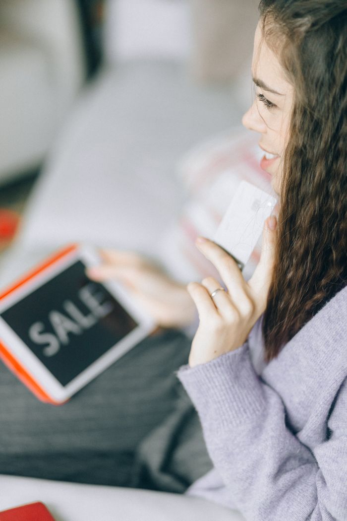 Woman holding a credit card and tablet with 'Sale' for online shopping.